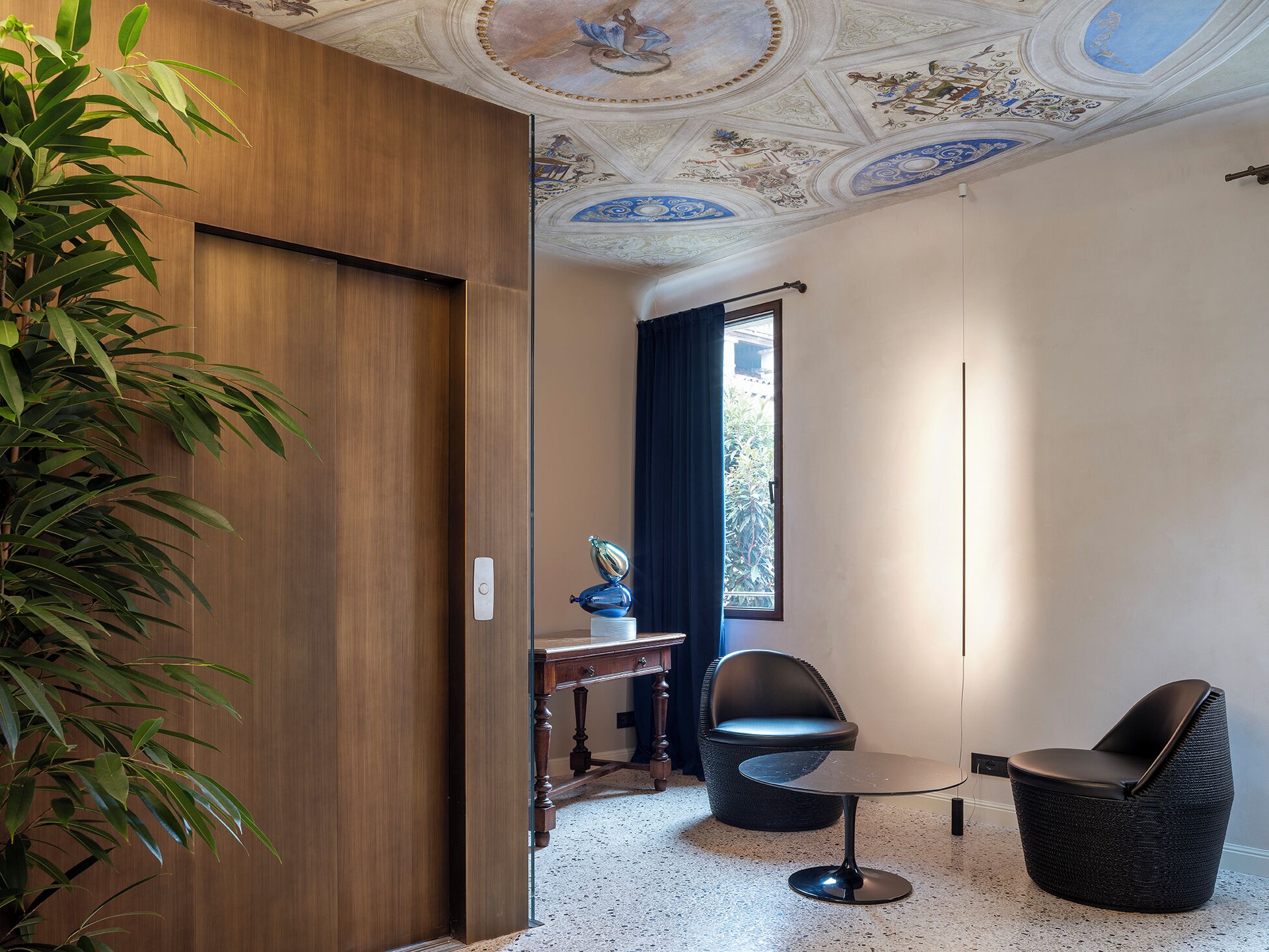 Una habitació amb una porta de fusta, una taula petita, dues cadires, un sostre decoratiu i una finestra amb cortines.