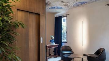 Una habitació amb una porta de fusta, una taula petita, dues cadires, un sostre decoratiu i una finestra amb cortines.