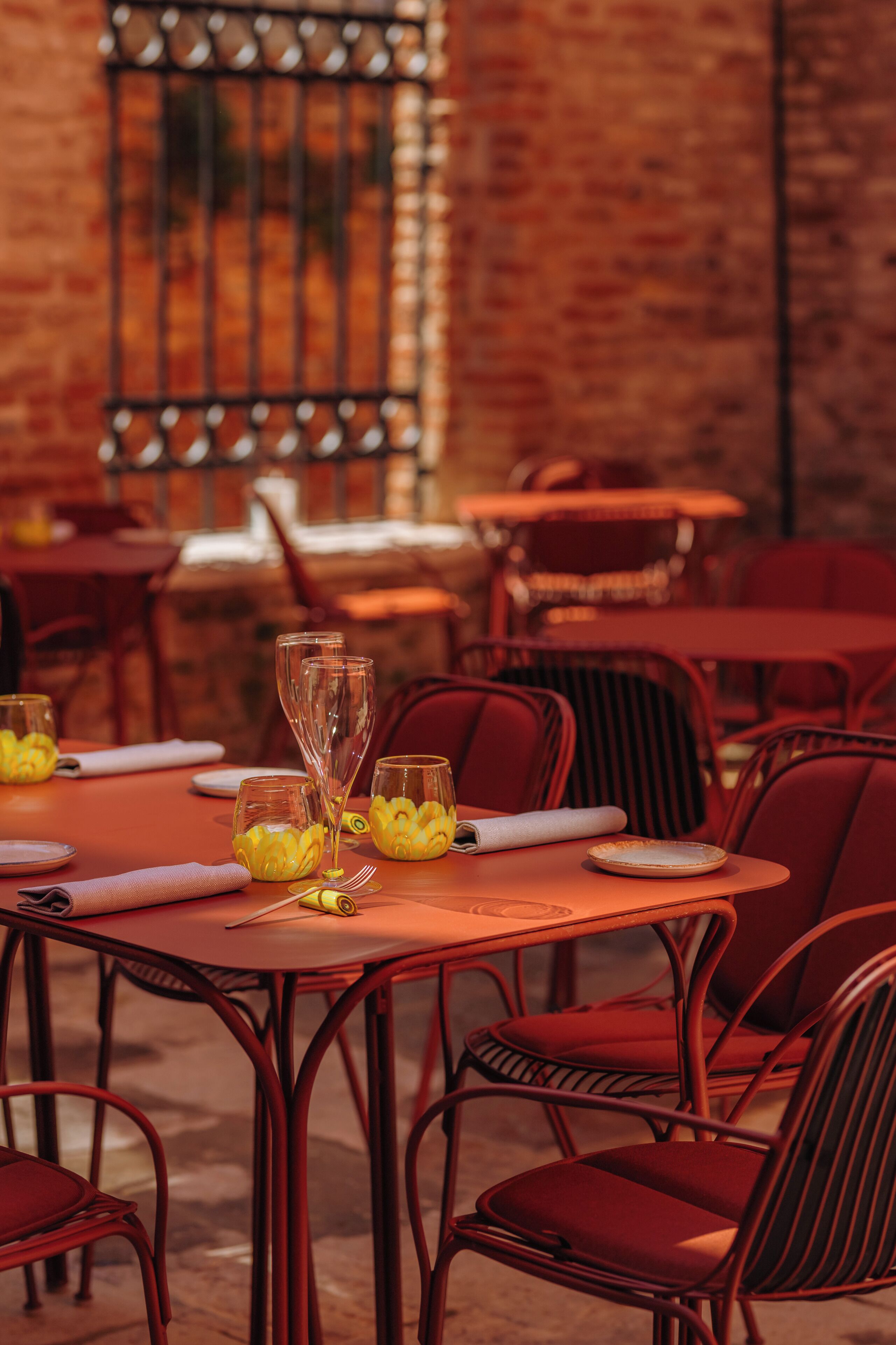 A restaurant setting with tables set for dining, featuring red chairs and a brick wall background.