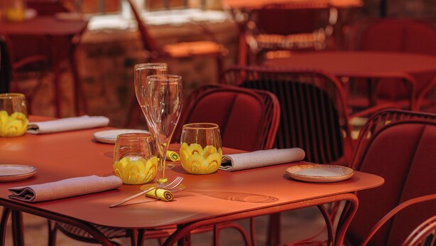 A restaurant setting with tables set for dining, featuring red chairs and a brick wall background. - Palazzetto My Venice (Venice)