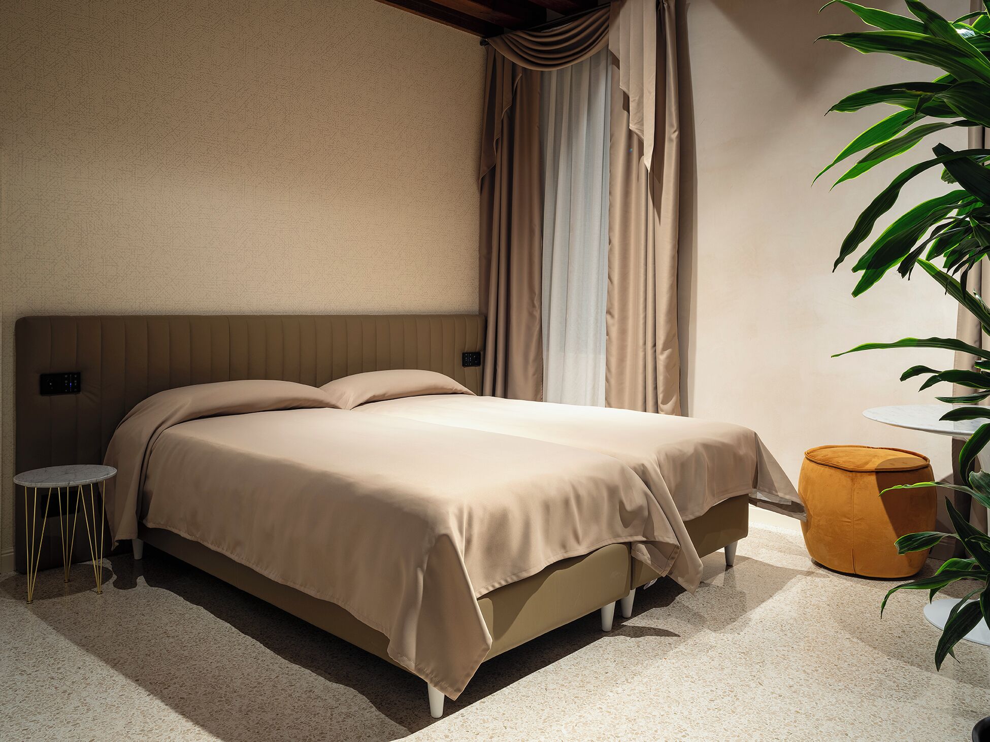 A bedroom with a bed, bedside tables, curtains, and a potted plant.