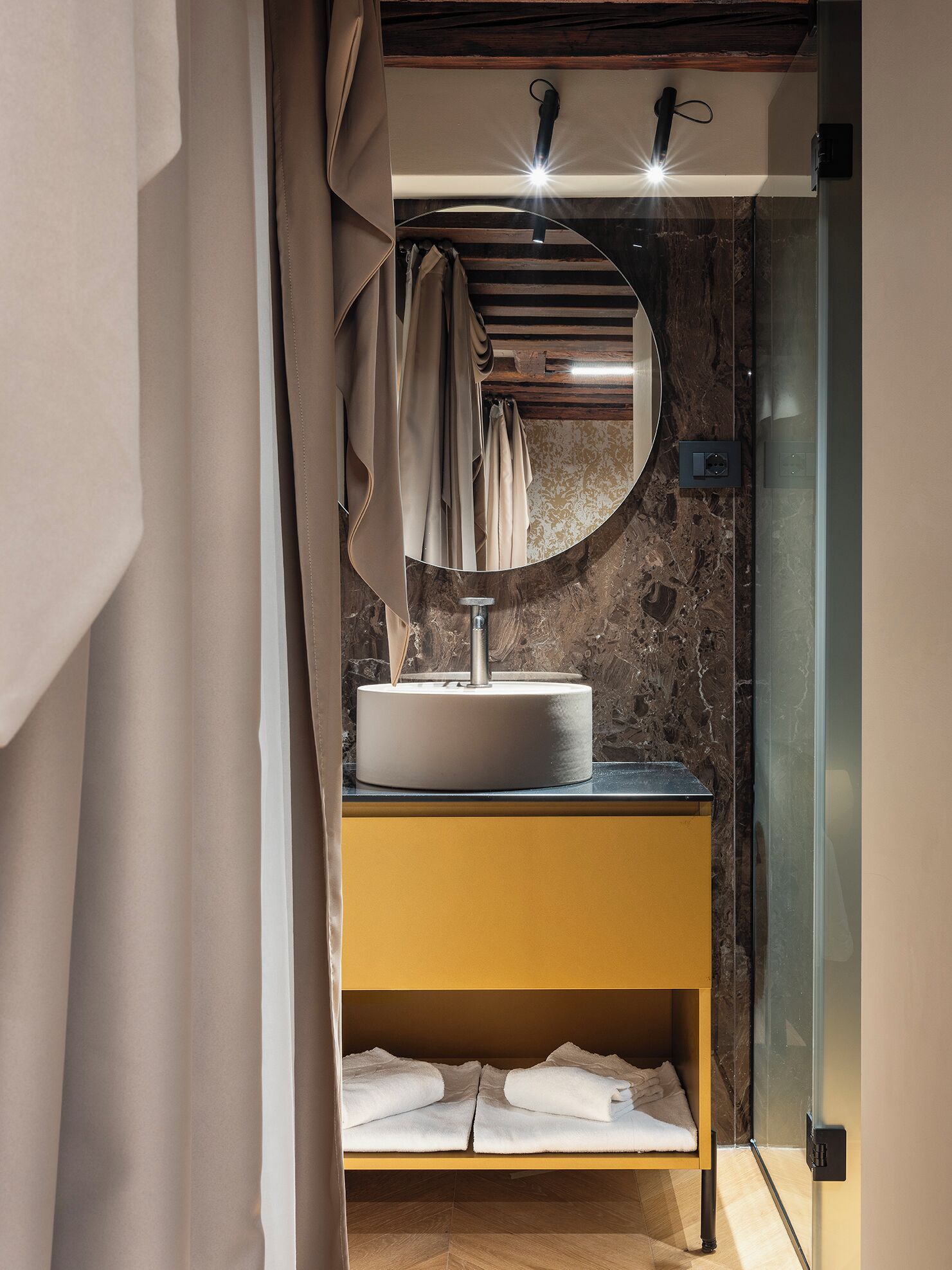 A modern bathroom with a round mirror, a sink, and a towel rack.