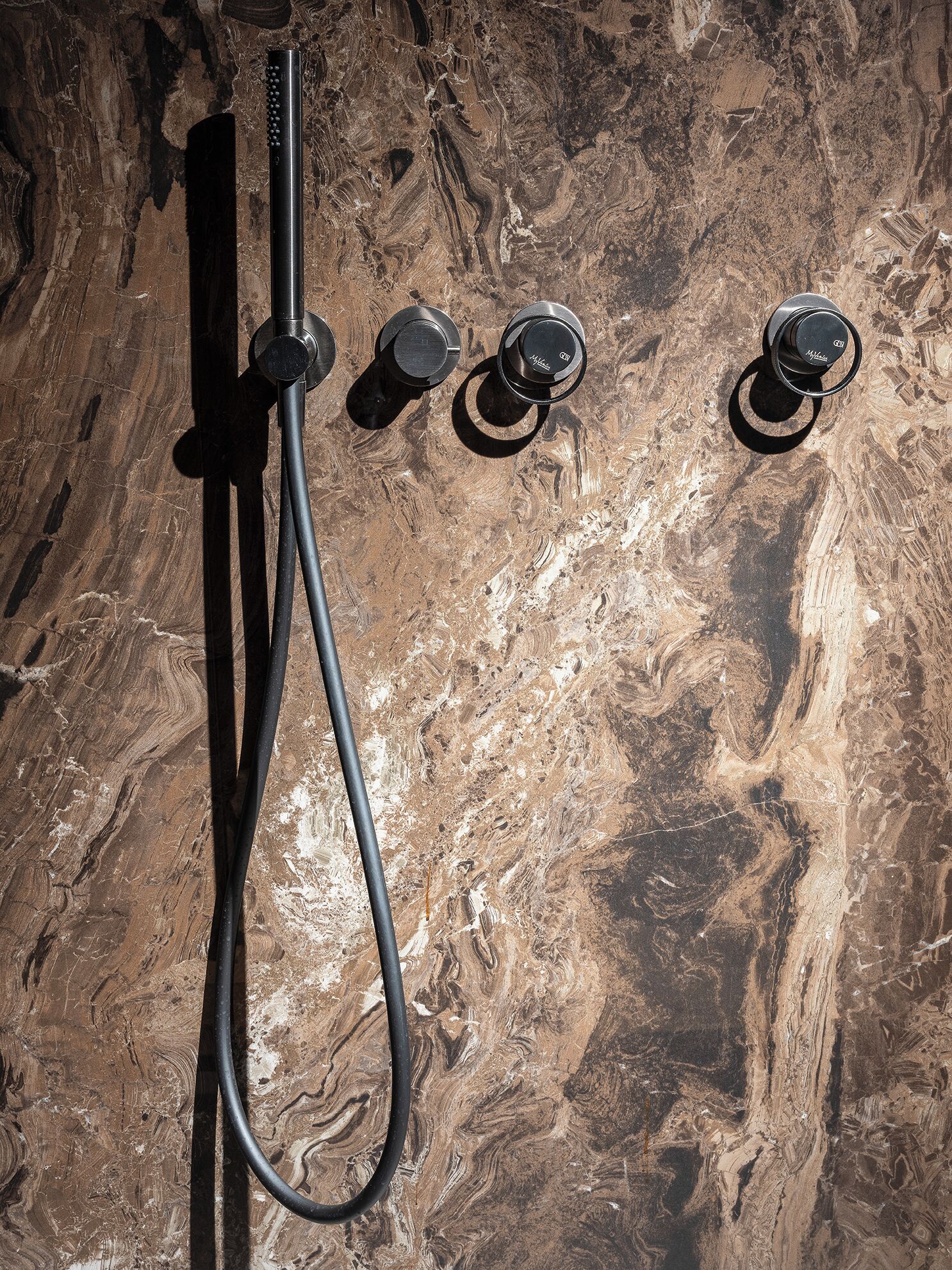 Une douche avec un mur en marbre en arrière-plan.