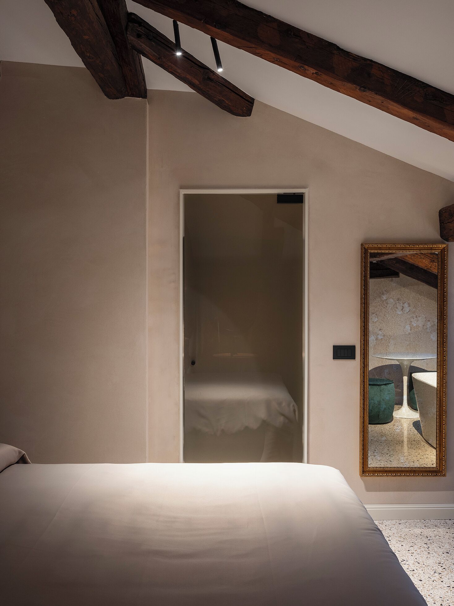 Un dormitorio con cama, viga de techo de madera, una puerta y un espejo con marco decorativo.