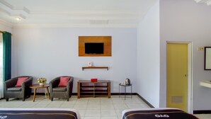 Een hotelkamer met twee eenpersoonsbedden, een tv aan de muur, een klein houten tafeltje met een rode schaal, twee fauteuils, en een gele deur.