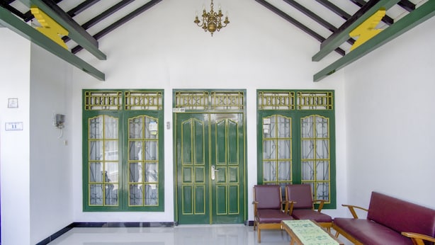 Een kamer met een groene deur, een kroonluchter en twee banken.