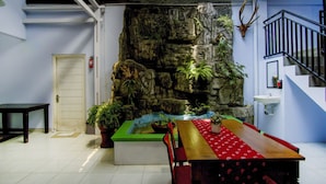 Een kamer met een eettafel, een rotswand met waterval, een trap en een deur.