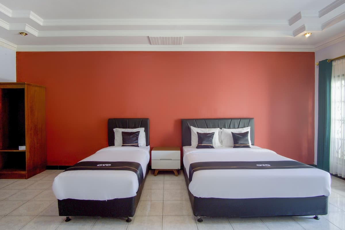 Une chambre d’hôtel avec deux lits, une armoire en bois et un mur d’accent de couleur rouge.