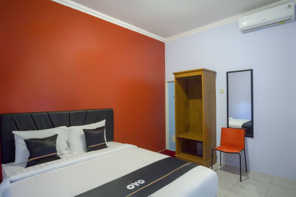 Une chambre d’hôtel avec un lit, une armoire, une chaise et un miroir.
