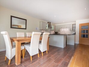 A modern kitchen with white cabinets, a wooden dining table with four chairs, and a large mirror on the wall.