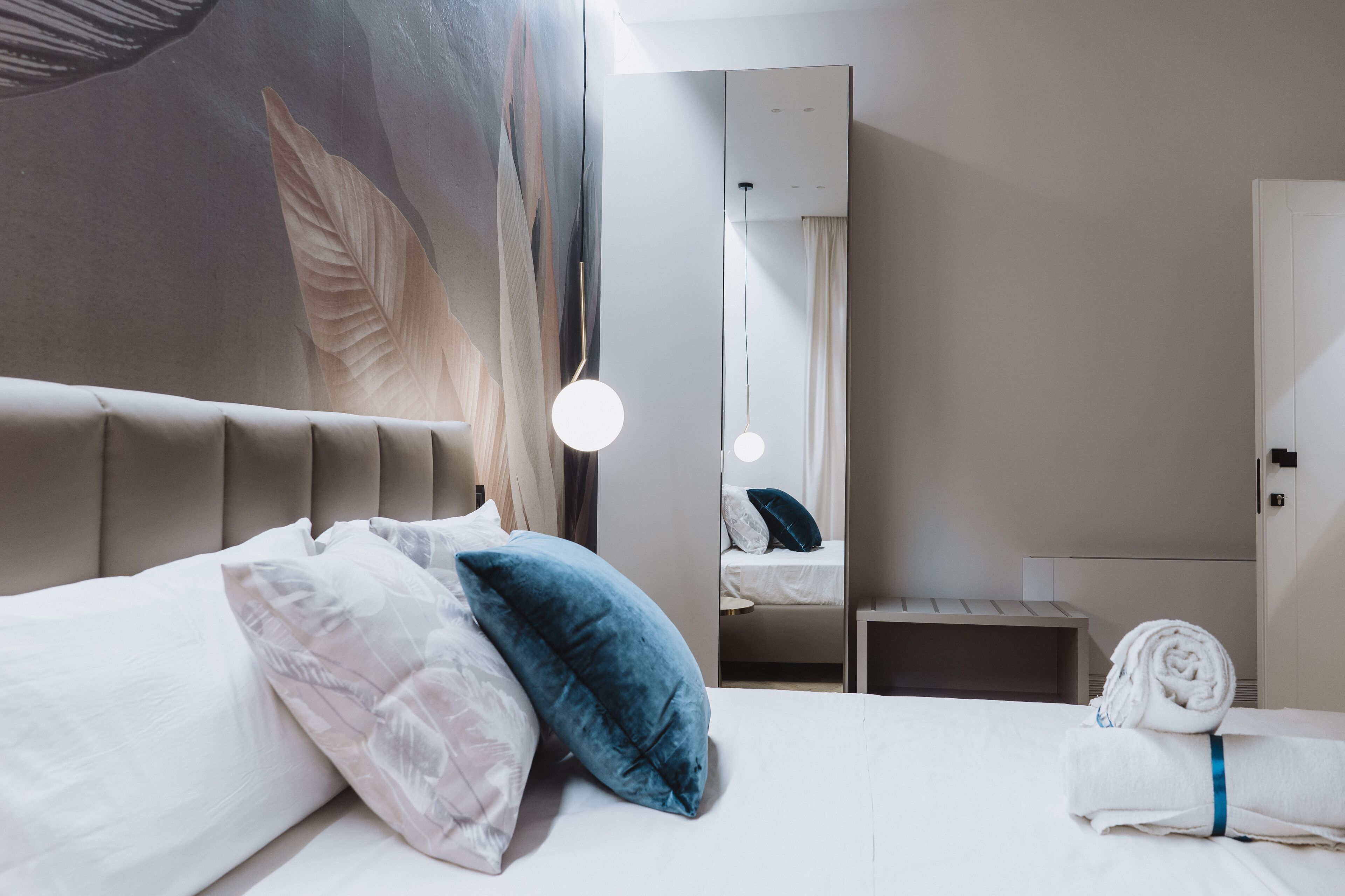 Ein Hotelzimmer mit einem großen Bett, einem Spiegel, einem Nachttisch und einer Wand mit Blattformen.