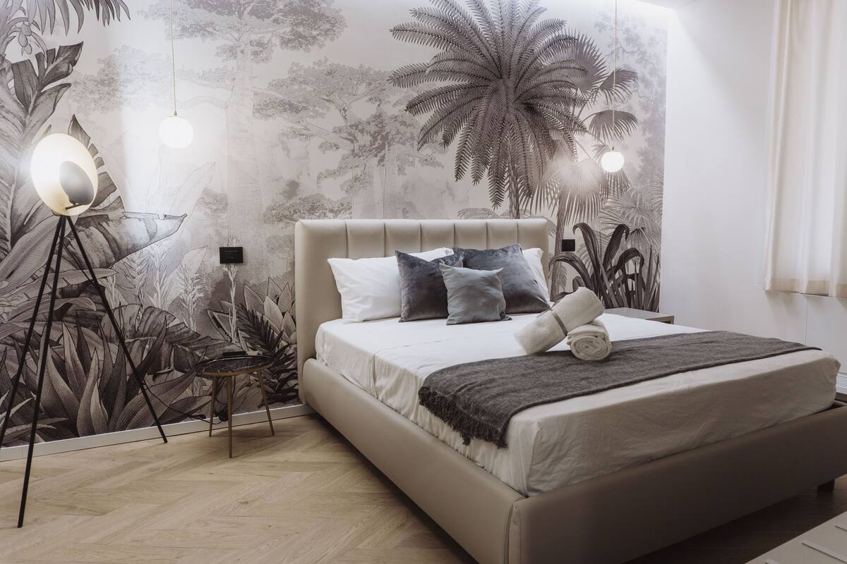 A bedroom with a large bed, a nightstand, a lamp, and a wall mural.