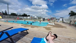 Ett poolområde med flera pooler, ett trädäck och en person som kopplar av i en solstol.