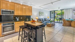 A modern kitchen with a central island, built-in appliances, and a dining area with wicker furniture. - 3-Min Walk to Beach! Ground Floor - No Resort Fee (Kihei)