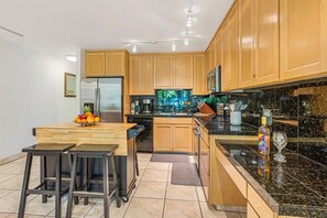 Eine moderne Küche mit Holzausstattung, einem Edelstahlkühlschrank, einer Kaffeemaschine und einer Obstschale auf der Arbeitsplatte.