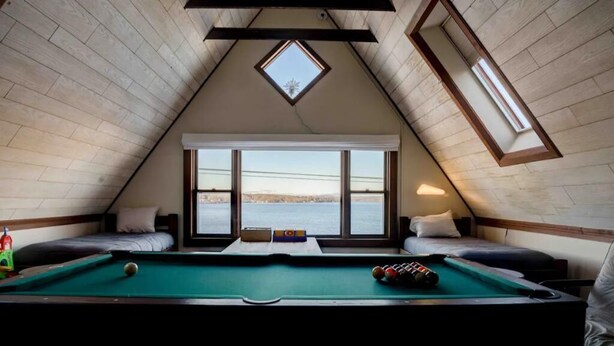 Una habitación acogedora con mesa de billar, dos camas, tragaluz y vista a un cuerpo de agua.
