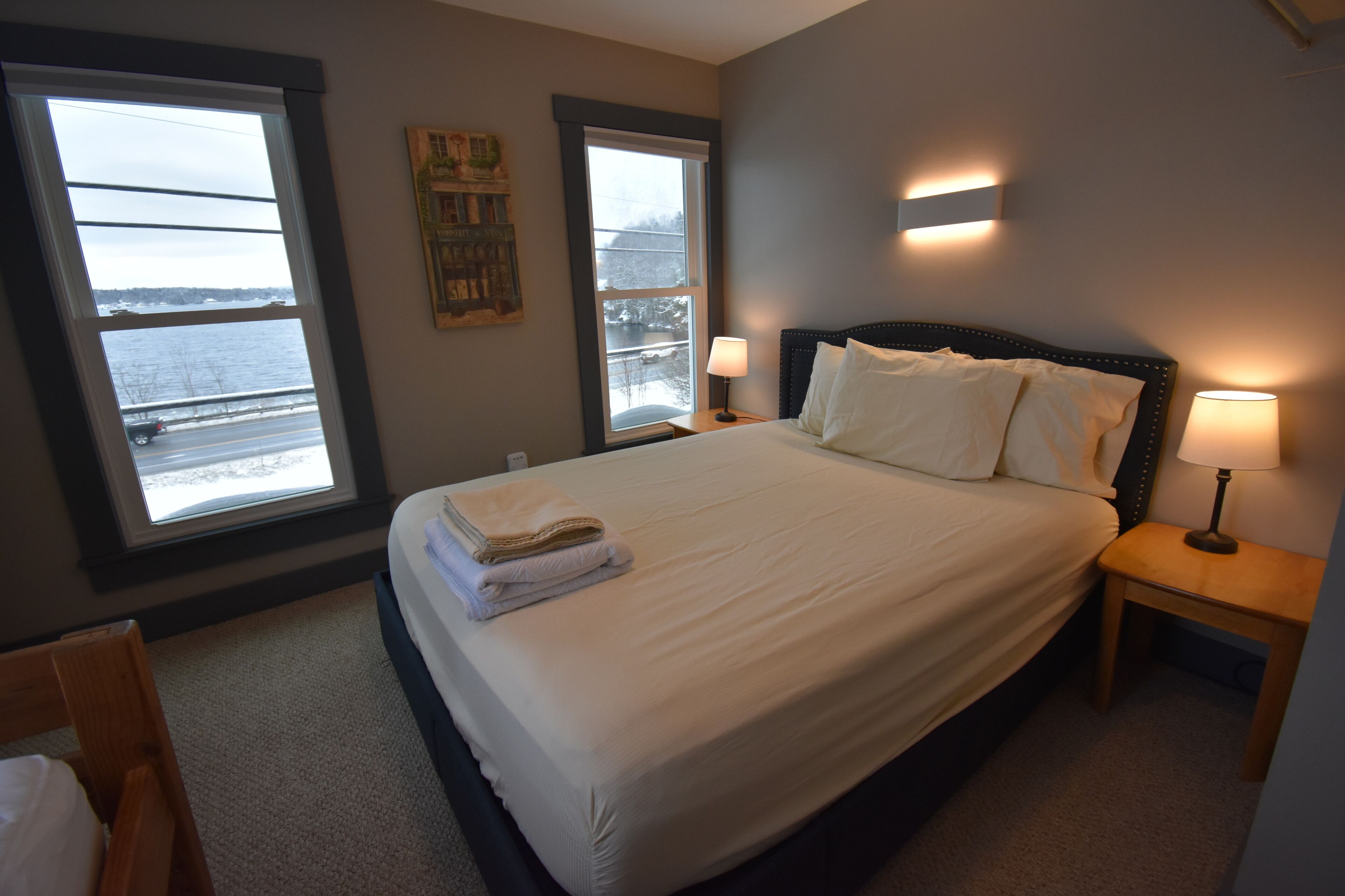 A neatly made bed with a folded towel, two bedside lamps, and a window with a view of a snowy landscape.