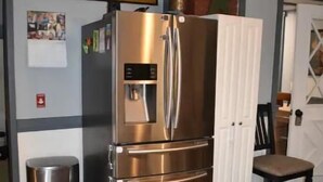 Un refrigerador de acero inoxidable en una cocina con piso de madera, un armario blanco y un letrero en la pared que dice 'General Store'.