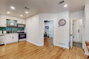 A modern kitchen with white cabinets, a microwave, and an oven. There is a clock on the wall and a door leading to another room.