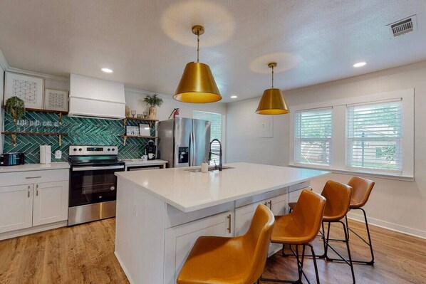 A modern kitchen with white cabinetry, stainless steel appliances, and a central island with bar stools.