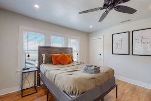Un dormitorio con cama, ventilador de techo, mesita de noche y cuadros decorativos.