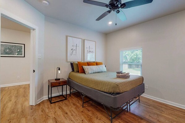 A bedroom with a bed, a nightstand, a ceiling fan, and a window with blinds.