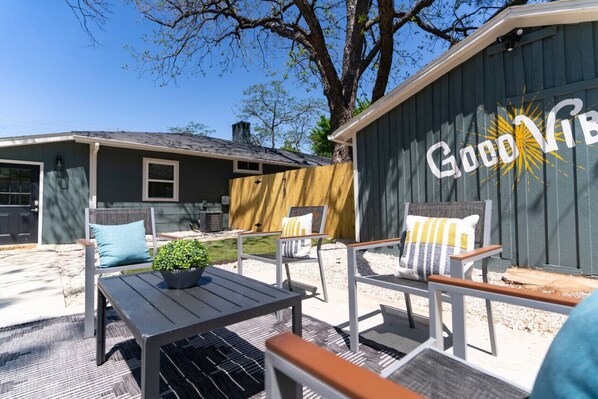 Ein Terrassenbereich im Freien mit Tisch und Stühlen, einem Holzzaun und einem Gebäude mit einem Schild 'Good Vibes'.