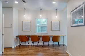 Un comedor con una mesa larga, cuatro sillas, luces colgantes y cuadros en las paredes.