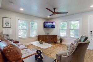 A living room with a brown leather couch, a grey armchair, a coffee table, and a flat-screen TV mounted on the wall.