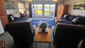 A living room with a large window, a wooden coffee table, two sofas, and a cabinet. - Cozy Red Door Cottage on Jordan Lake - Pontoon Boat Rental available (Lake Odessa)