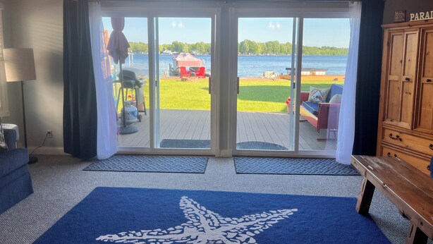 A room with a large sliding glass door leading to a deck with a view of a lake. - Cozy Red Door Cottage on Jordan Lake - Pontoon Boat Rental available (Lake Odessa)
