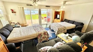 A compact room with two beds, a sofa, a TV, and a view of the outdoors. - Cozy Red Door Cottage on Jordan Lake - Pontoon Boat Rental available (Lake Odessa)