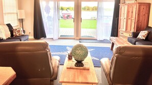 A living room with two leather sofas, a coffee table, and a cabinet. There is a sliding glass door leading to a backyard. - Cozy Red Door Cottage on Jordan Lake - Pontoon Boat Rental available (Lake Odessa)