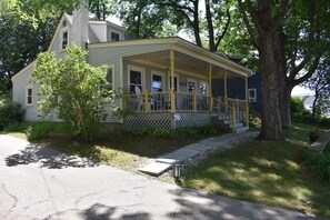 Ein zweistöckiges Haus mit Veranda, kleinem Vorgarten und einem Baum.