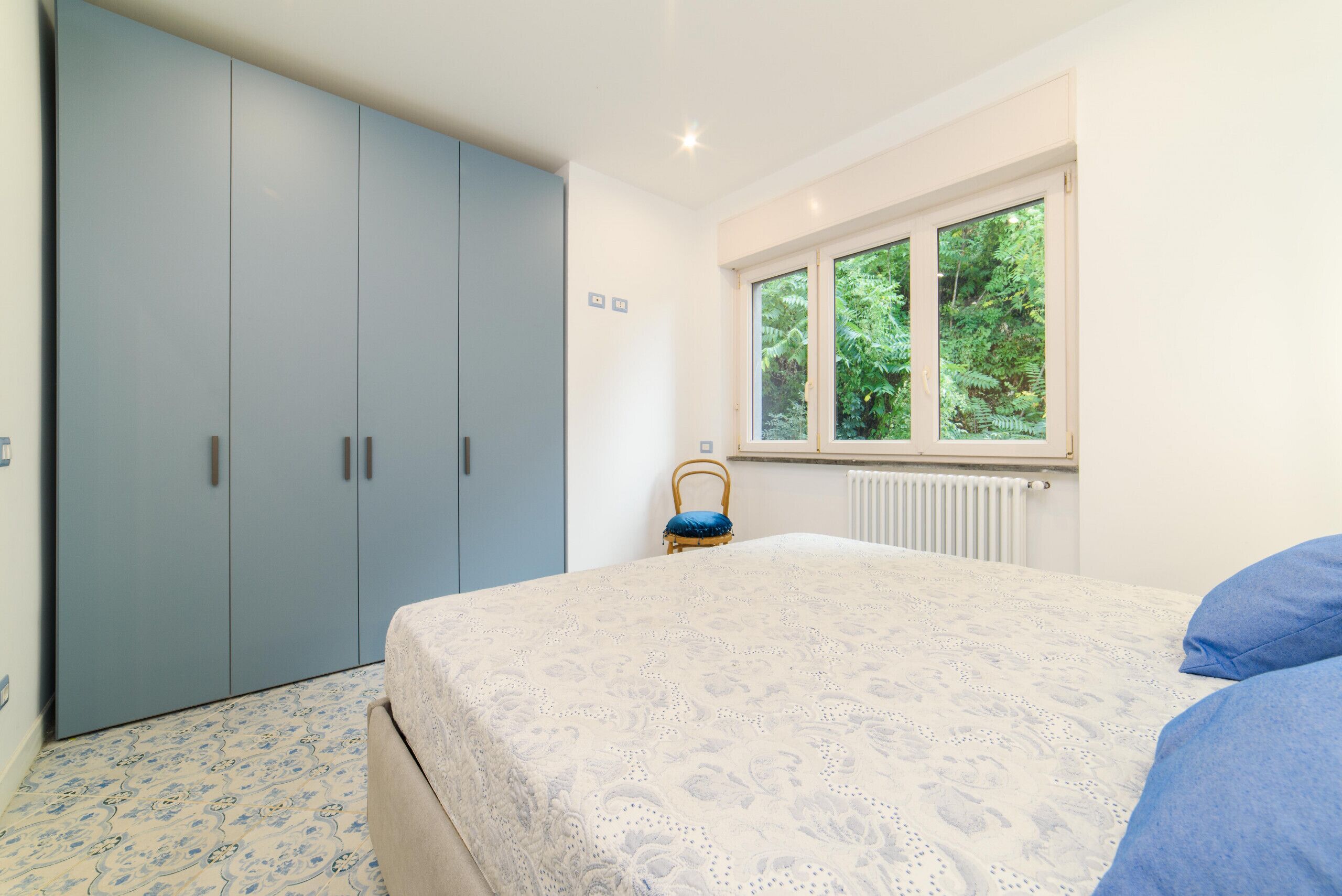 A bedroom with a bed, a wardrobe, and a window with a view of greenery.