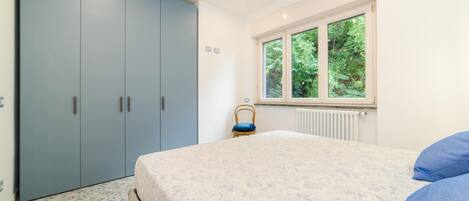 A bedroom with a bed, a wardrobe, and a window with a view of greenery.