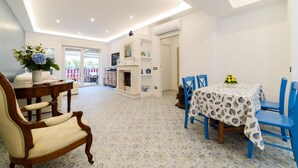 A dining area with a table set for four, surrounded by blue chairs. There is a wooden chair with a cream cushion to the left. The room has a tiled floor with a blue pattern and white walls. - Estate4home - The Attic (Sorrento)