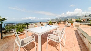 A terrace with a white table and chairs, a view of the sea, and a mountainous landscape in the background. - Estate4home - The Attic (Sorrento)