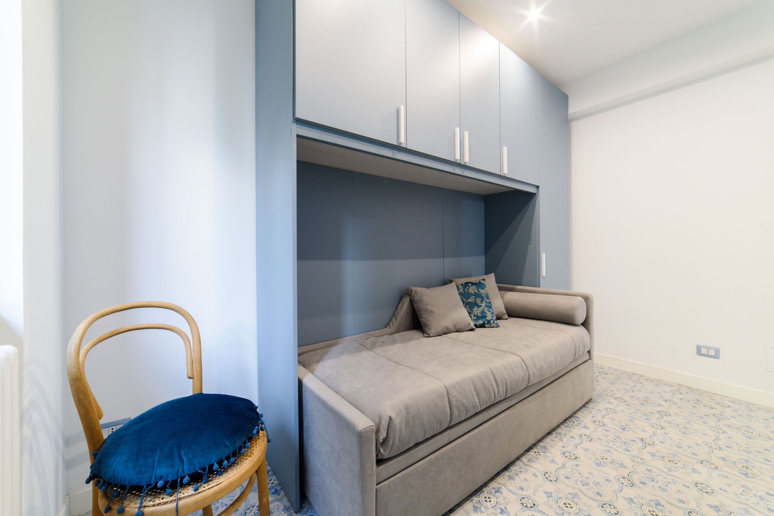 Una habitación con un sofá, una silla con un cojín azul y un armario con pomos blancos.
