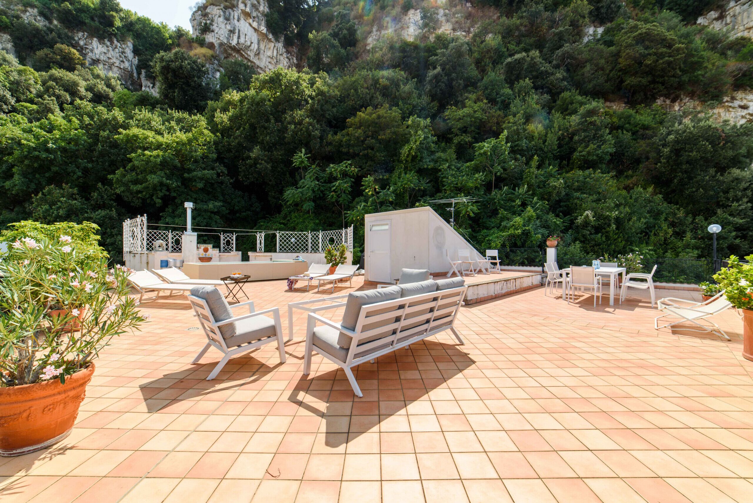 A rooftop terrace with outdoor seating, a barbecue area, and a view of a forested hillside.