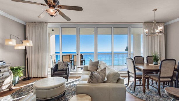 A spacious living room with a large window overlooking the ocean, a ceiling fan, and a dining area with a view. - 🌊Silver Beach 603E | Beach Front | Upscale + Disc. Beach Service (Destin)