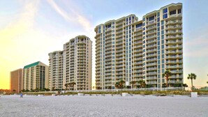 A beachfront hotel with multiple high-rise buildings, a sandy beach in the foreground, and palm trees. - 🌊Silver Beach 603E | Beach Front | Upscale + Disc. Beach Service (Destin)