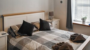 A neatly made bed with a plaid bedspread, two black pillows, and a bedside lamp on a nightstand.