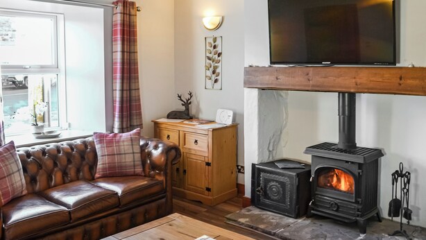 A cozy living room with a leather sofa, wooden coffee table, and a stone fireplace with a wood-burning stove.