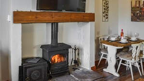 A cozy room with a wood-burning stove, a television mounted above it, and a dining table set for four.