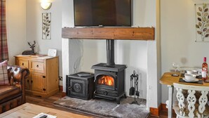 A cozy living room with a wood-burning stove, a television mounted above it, a wooden cabinet, and a dining area with a table and chairs.