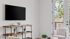 A modern living room with a flat-screen TV, a wooden console table, two chairs, a coffee table, and a ceiling fan.
