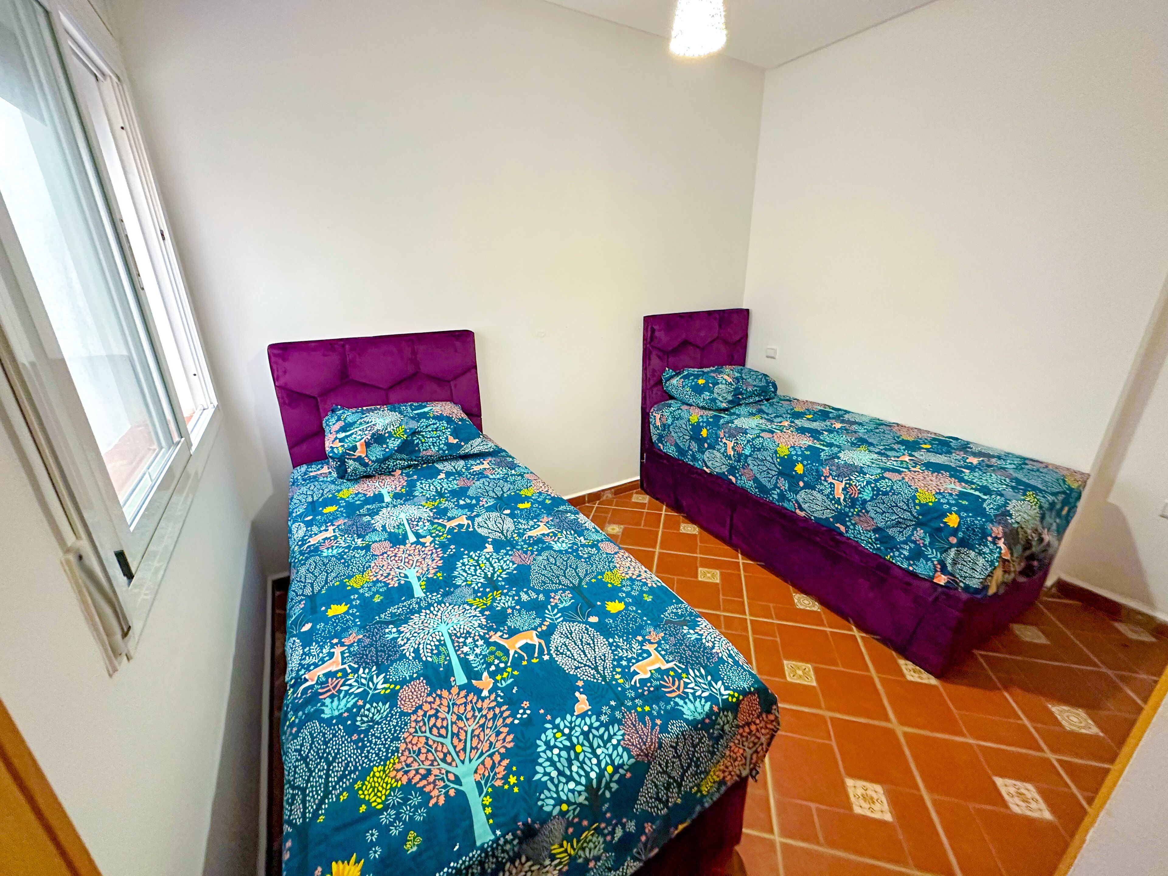 Een kamer met twee bedden, elk met een paars hoofdeinde en blauw bloemenbeddengoed.