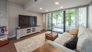 Een moderne woonkamer met een grote televisie, witte meubels en uitzicht op de omgeving.