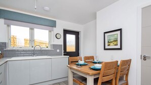 Una cocina moderna con comedor, que incluye una mesa y sillas de madera, un ventanal con vistas, y un reloj en la pared.